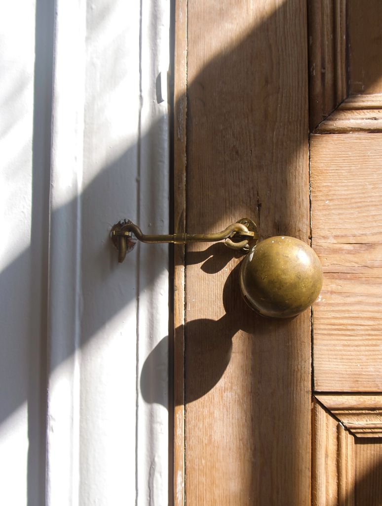 A detailed image of a brass door knob with a latch, casting shadows on a wooden door.